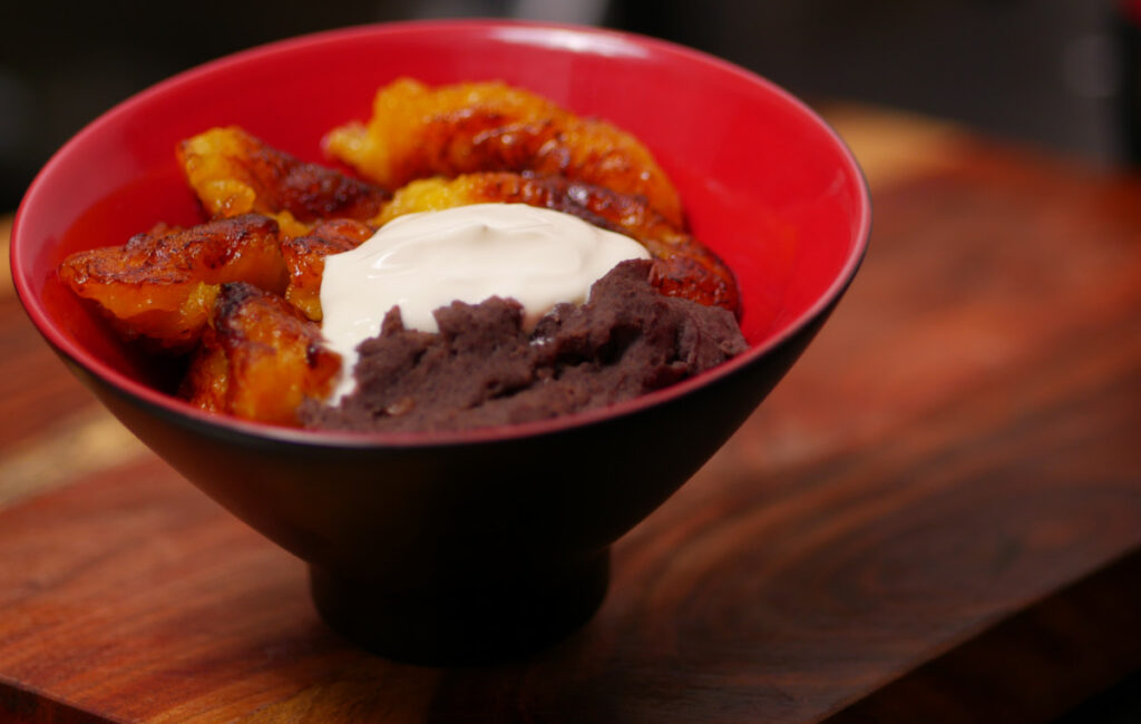 A small bowl of fried plantains slices with refried beans and a dollop of sour cream.